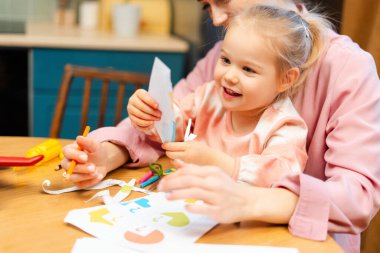 Mutlu küçük kız ve anne kağıt şekilleri kesiyorlar, el işi sırasında kaynaşıyorlar.