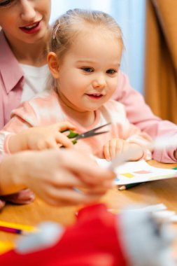 Çocuğun elleri makas tutuyor, zanaat faaliyetleri sırasında annesiyle kağıt kesiyor.