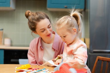 Bir zanaat projesi üzerine anne-kız kaynaşıyor, evde makasla kağıt kesiyor.