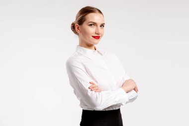 Beyaz bir arkaplanda kollarını kavuşturarak poz veren iş kadını, güven ve başarıyı temsil ediyor.