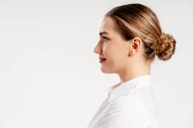 Zarif yan profili olan zarif bir kadın, temiz bir arkaplanda beyaz gömlek giyiyor.