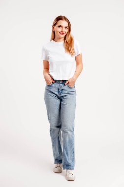 Gülümseyen kadın temiz bir stüdyo arka planında kot pantolon ve beyaz t-shirt ile poz veriyor.