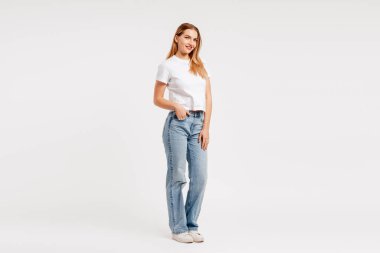 Kusursuz beyaz bir arka planda duran, gülümseyen ve kameraya bakan genç bir kadın.