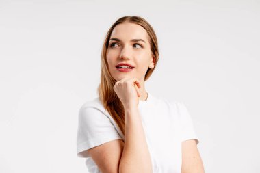 Düşünen genç bir kadın, beyaz arka planda düşünceli bir ifadeyle başka yere bakıyor.