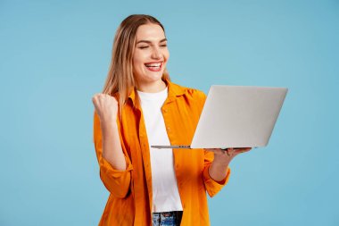 Heyecanlı genç kadın online başarısını dizüstü bilgisayarla kutluyor, zaferde yumruğunu sıkıyor.