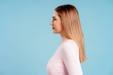 İleriye bakan genç bir kadın, profilini gösteriyor ve uzun sarı saçlı, temiz bir geçmişi var.