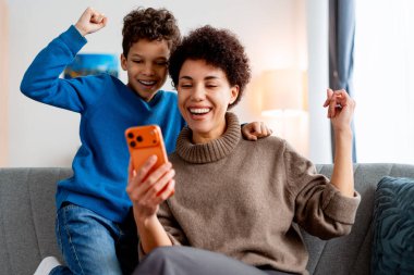 Mutlu anne ve oğul evde cep telefonuna bakarken heyecanla tepki veriyorlar.