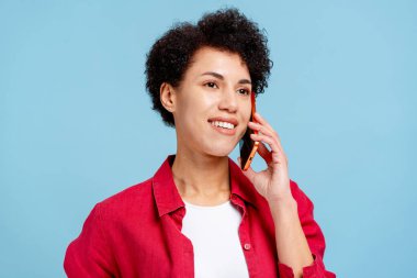 Cep telefonuyla konuşurken gülümseyen, teknolojiyle iletişim kuran genç bir kadın.