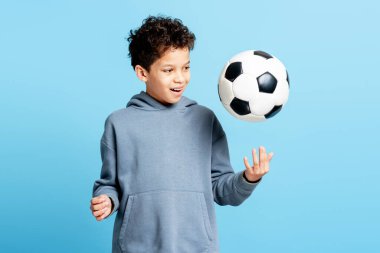 Mavi arka planda izole bir şekilde futbol oynayan küçük sevimli erkek oyuncunun portresi. Spor konsepti