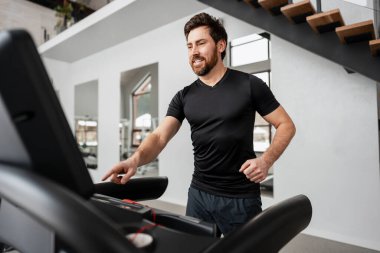 Spor salonunda koşu bandında egzersiz yapan bir adam, kardiyo eğitimi için egzersiz programı hazırlıyor.