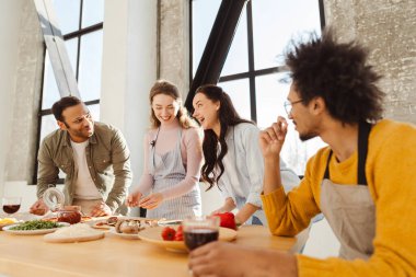 Bir grup mutlu, pozitif, çok ırklı arkadaş birlikte yemek pişiriyor ve modern mutfakta pizza yapıyorlar. Yiyecek konsepti