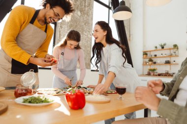 Gülümseyen, çok uluslu bir grup kadın ve erkek birlikte yemek pişiriyor ve modern stil mutfağında yemek yapıyorlar. Arkadaşlık kavramı