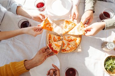 Üst tabaka, masada oturan farklı arkadaşlar, modern pizzadaki ellere odaklanmış pizza parçaları. Yiyecek konsepti