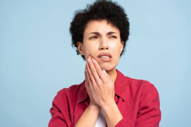 Afro-Amerikalı bir kadın diş ağrısı çekiyor mavi arka planda izole bir şekilde başka tarafa bakıyor. Diş bakımı, dişçilik konsepti