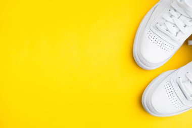 Sarı arka planda bir çift şık beyaz spor ayakkabısı.