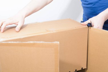 Caucasian man holding sharp steel box cutter knife with open cardboard box