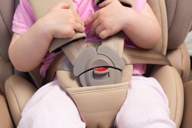 Faceless small baby sitting in special car seat with safety seatbelts