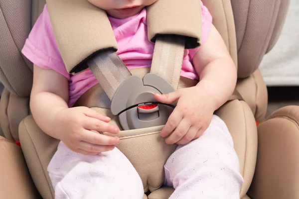 Faceless small baby sitting in special car seat with safety seatbelts