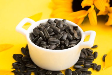 Closeup view of black sunflower seeds in white ceramic bowl with flowers