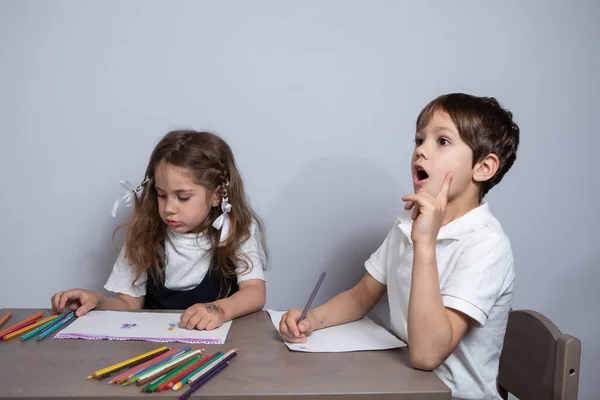 Das Mädchen und der Junge sitzen am Tisch und halten Bleistifte in der Hand. Sie zeichnen. — Stockfoto