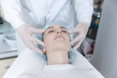 Genç güzel kız güzellik salonunda kanepede uzanıyor ve yüz masajı yaptırıyor..