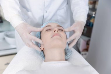 Genç güzel kız güzellik salonunda kanepede uzanıyor ve yüz masajı yaptırıyor..