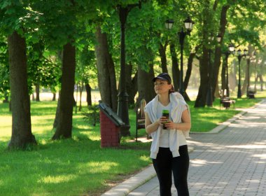 Bir yaz sabahı parkta koştuktan sonra termo bardaktan çay içen genç bir kadın.