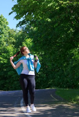 Koştuktan sonra kız parkta yürür ve termo bardaktan çay içer..