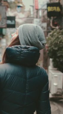 Genç kadın Tokyo sokaklarını keşfediyor, gelenek ve modernliği harmanlıyor, kışın şehrin özünü yakalıyor. Samimi kıyafetleri şehir macerasına sıcaklık katıyor.