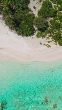 Maldivler içinde beyaz kumsalda yürüyen bir kadının havadan görünüşü turkuaz sular ve palmiye ağaçları lüks bir tatil için bir cennet yaratıyor.
