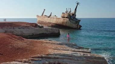 Genç kız ve diğerleri kayalık Paphos kıyılarında mahsur kalan Edro III kargo gemisini açık mavi Akdeniz sularına ve parlak bir yaz gökyüzüne, seyahat ve doğa çatışmasına karşı izliyorlar.