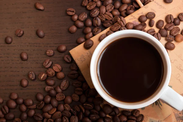 Xícara de café e grãos de café em mesa marrom escuro — Fotografia de Stock