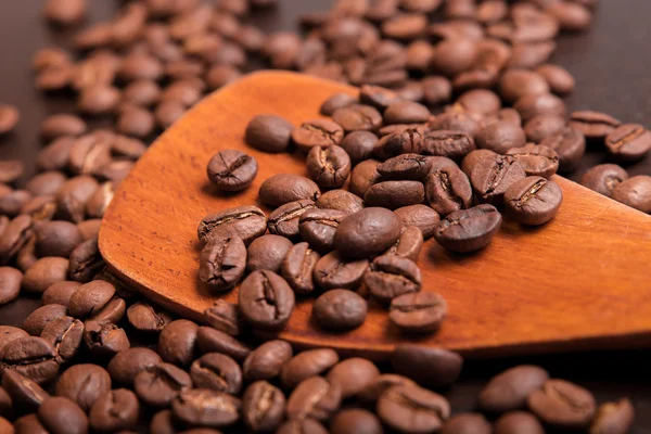 Kaffebönor i en trä skopa på bruna bord — Stockfoto