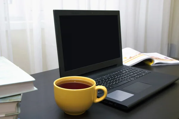 İşyeri: dizüstü bilgisayar, kitap ve çay siyah masa üzerinde