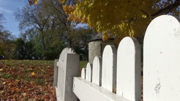 Herfst landschap met vallende bladeren, picket fences en een stenen shack — Stockvideo