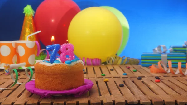 Tort urodzinowy z świece rustykalne drewniane tabela z tłem kolorowe balony, prezenty, kubki plastikowe i cukierki z niebieską ścianą, w tle — Zdjęcie stockowe