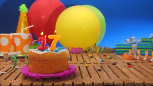 Bolo de aniversário com velas na mesa de madeira rústica com fundo de balões coloridos, presentes, copos de plástico e doces com parede azul no fundo — Fotografia de Stock