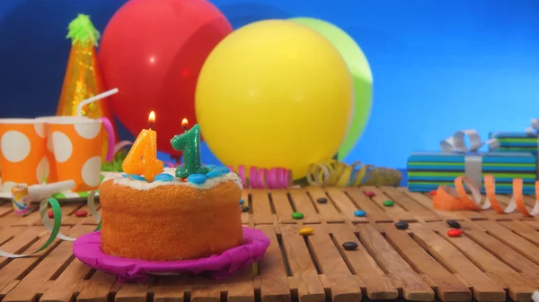 Születésnapi torta gyertyákkal a rusztikus, fából készült asztal háttér színes lufi, ajándékok, műanyag pohár és cukorka a kék falon a háttérben — Stock Fotó