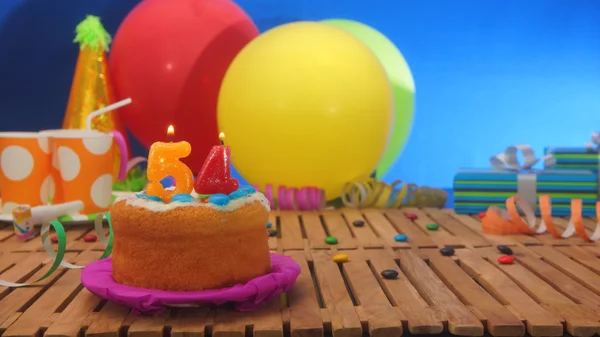 Bolo de aniversário com velas na mesa de madeira rústica com fundo de balões coloridos, presentes, copos de plástico e doces com parede azul no fundo . — Fotografia de Stock