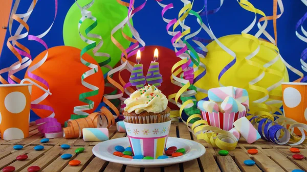 Urodziny ciastko z palące na rustykalne drewniany stół z tłem kolorowe balony, kubki plastikowe i cukierki z niebieską ścianą, w tle — Zdjęcie stockowe