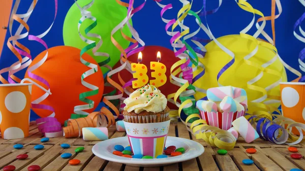 Urodziny ciastko z palące na rustykalne drewniany stół z tłem kolorowe balony, kubki plastikowe i cukierki z niebieską ścianą, w tle — Zdjęcie stockowe