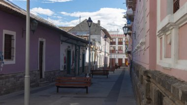 Latacunga, Cotopaxi / Ekvador - 5 Haziran 2021: Güneşli bir günde Letacunga şehir merkezindeki eski dar bir sokakta bankta oturan gençler