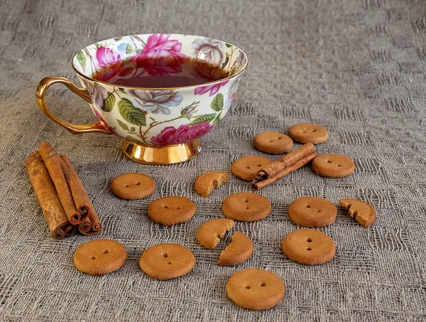 Taza de té con galletas y canela sobre mantel — Foto de Stock