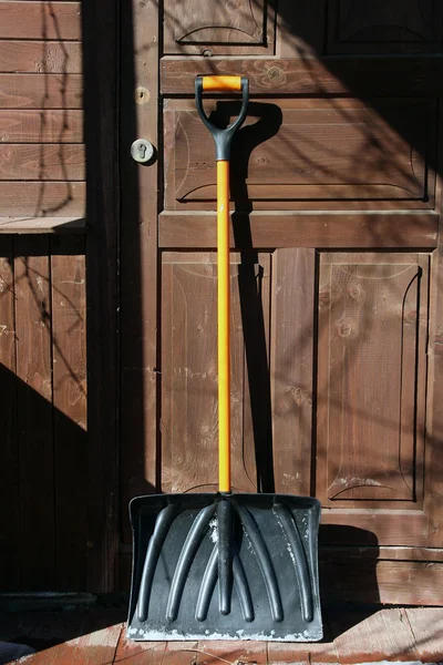 siyah plastik kar küreği ahşap kapıda turuncu saplı