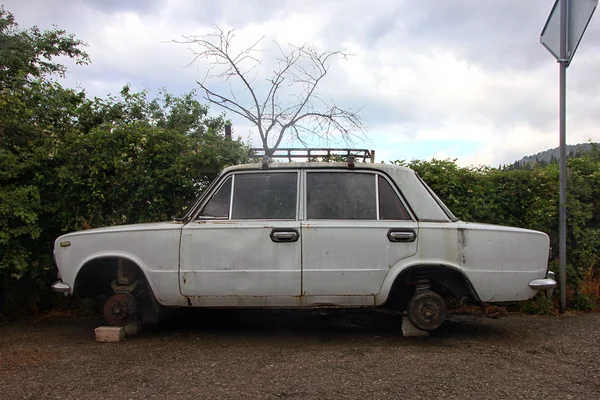 Viejo coche blanco oxidado sin ruedas está en la vista lateral de ladrillos —  Fotos de Stock