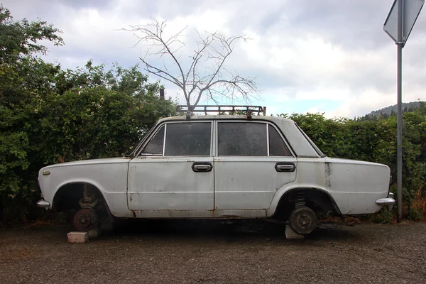 Old white rusty car without wheels is on the bricks side view — Stock Photo, Image