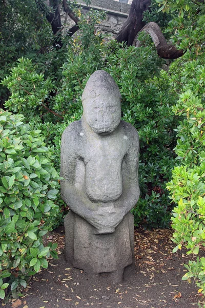 Маленький серый каменный гуманоидный идол в зеленом парке — стоковое фото