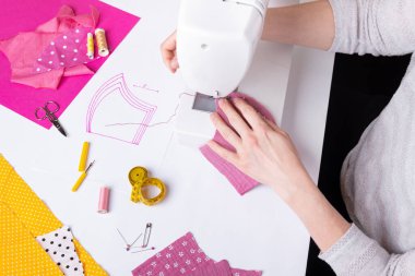 Kadın elleri, koronavirüs pandemisi sırasında pembe kadın yüzü maskesi dikmek için dikiş makinesi kullanıyor. Tıbbi malzeme sıkıntısı nedeniyle yerli dikiş.