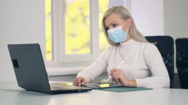 İnternette bilgisayar ve tablet kullanan koruyucu maskeli genç beyaz kız internette ya da işte öğreniyor. Ofiste masada oturan kadın.. 