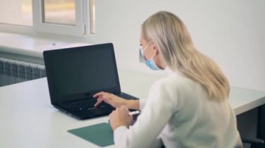 Koruyucu maske takmış, internette bilgisayar ve tablet kullanarak internetten öğrenen beyaz bir genç kız. Ofiste masada oturan kadın.. 